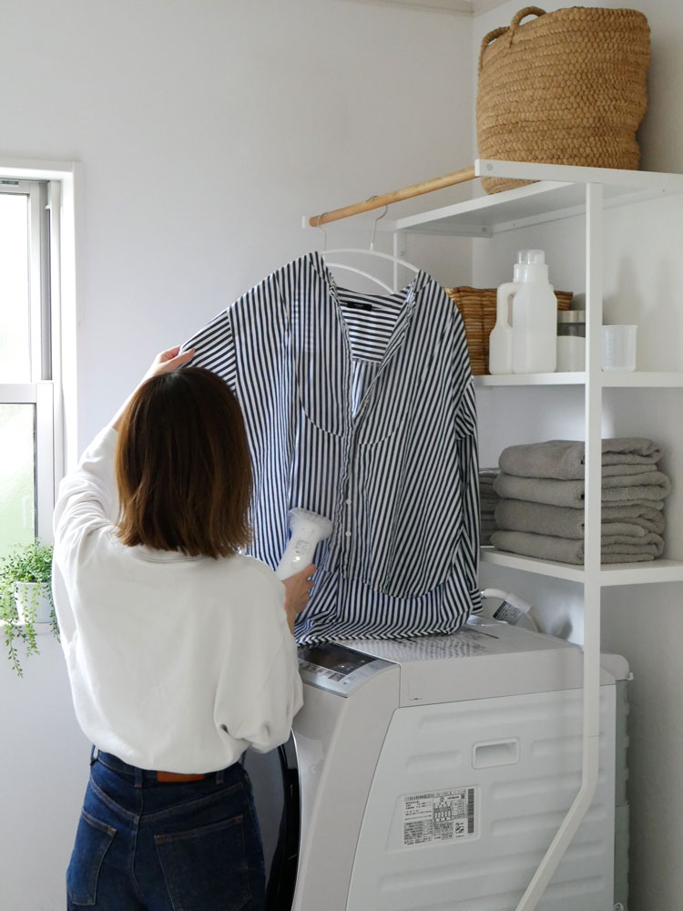 tower/Yamazaki製の立て掛けランドリーシェルフ。スチール製の本体に複数の棚と天然木のハンガーバーが備わり、家庭用洗濯機の横に設置された収納ユニット。